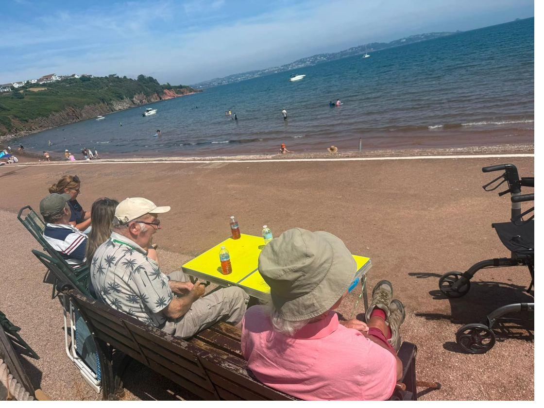 Sitting on a bench with a table of drinks, looking out across the bay at Broadsands