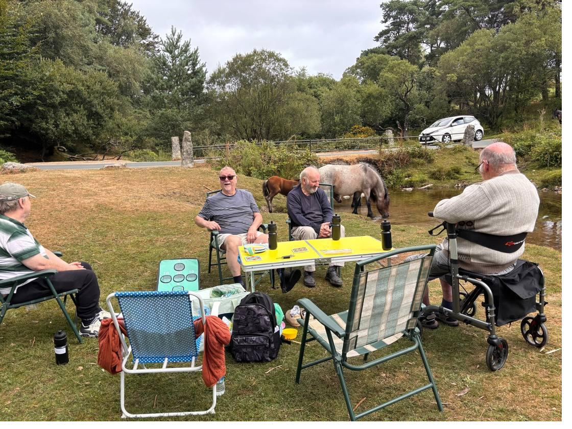 Playing cards at a folding table on Dartmoor while two ponies drink from the river behind