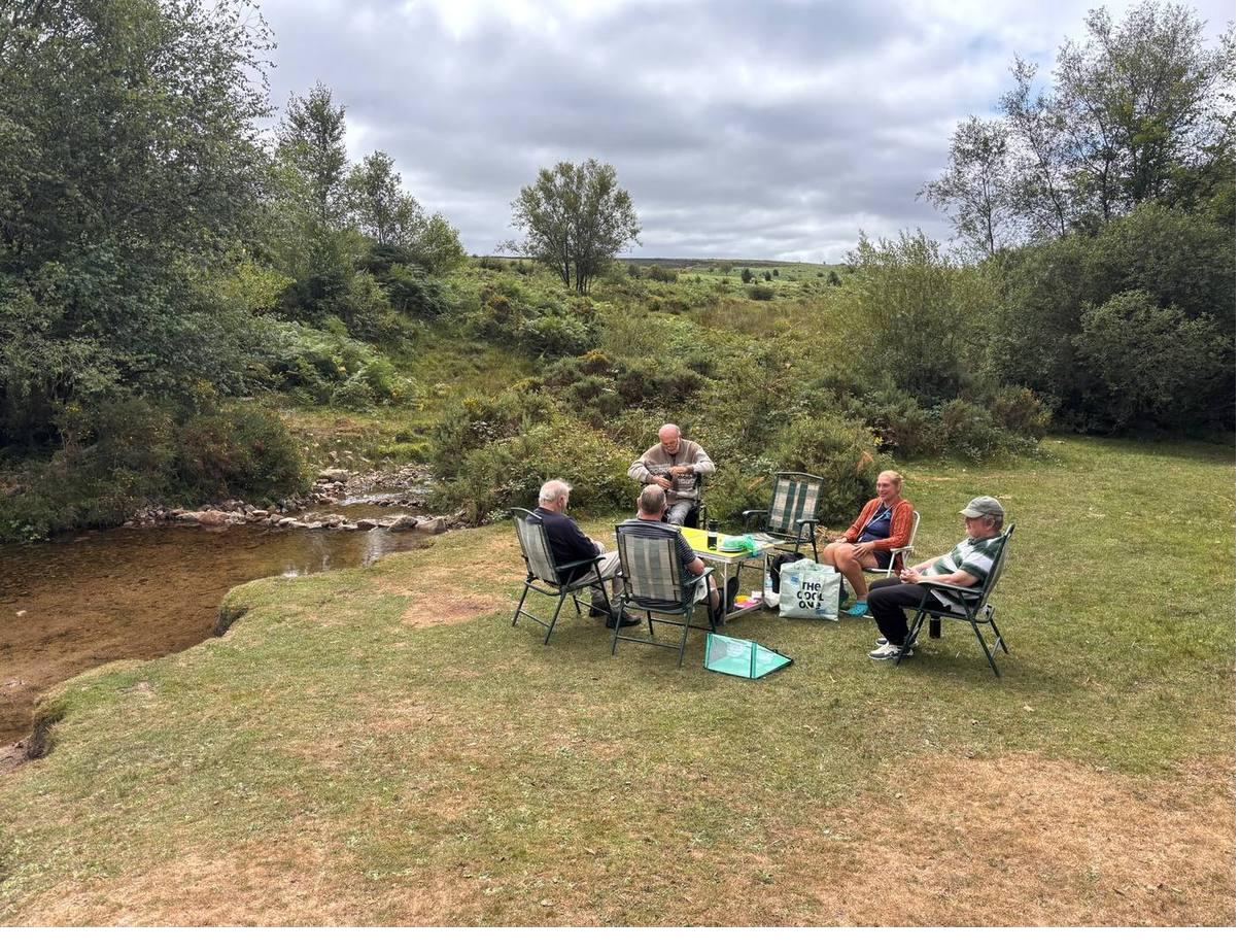 The group sitting out in camping chairs beside a shallow stream on Dartmoor