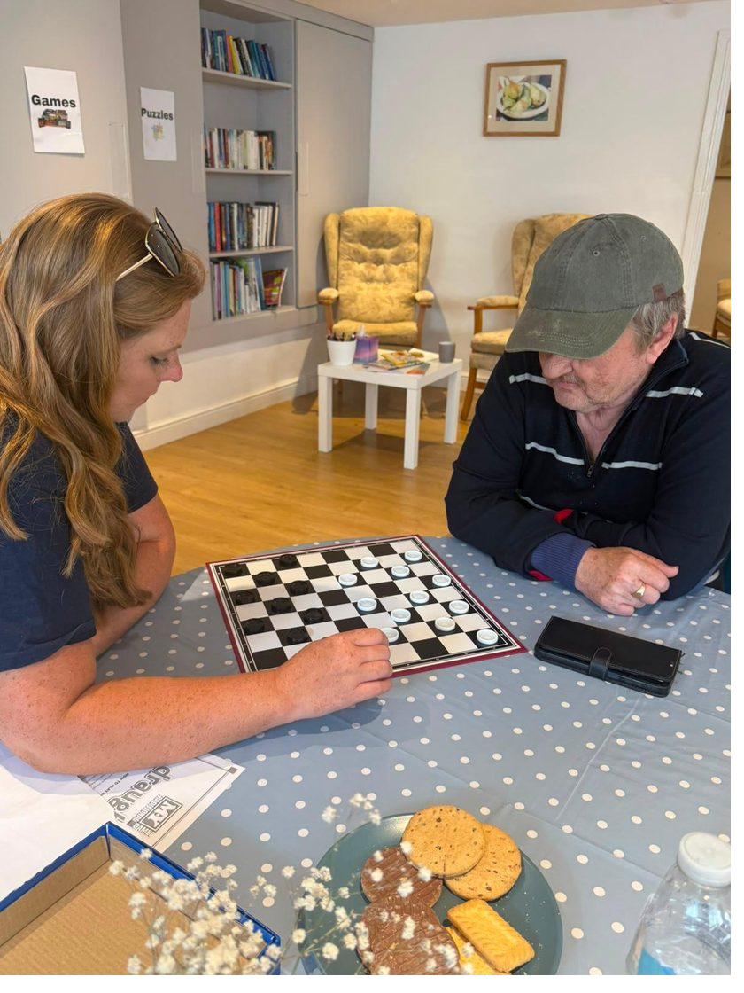 A member of staff and a gentleman playing a game of draughts together at one of the tables