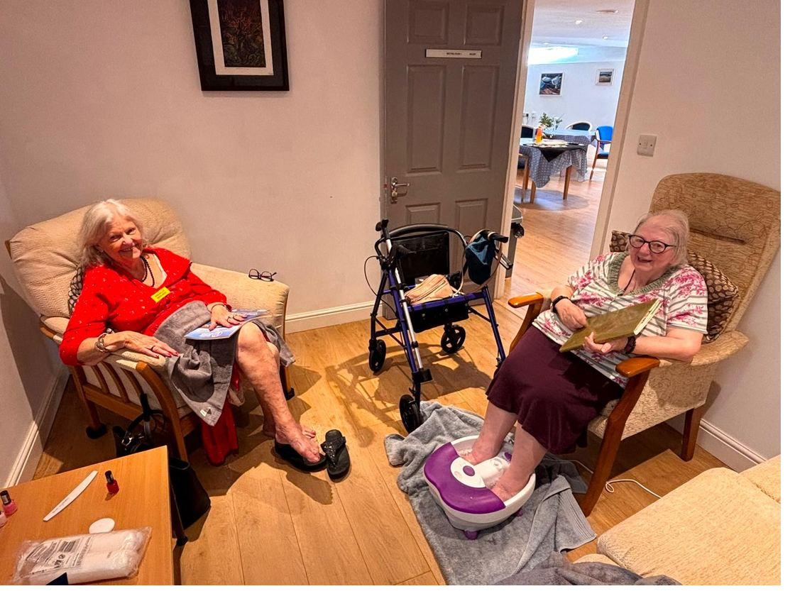 Two ladies laughing together during a pamper session, one with her feet in a foot spa