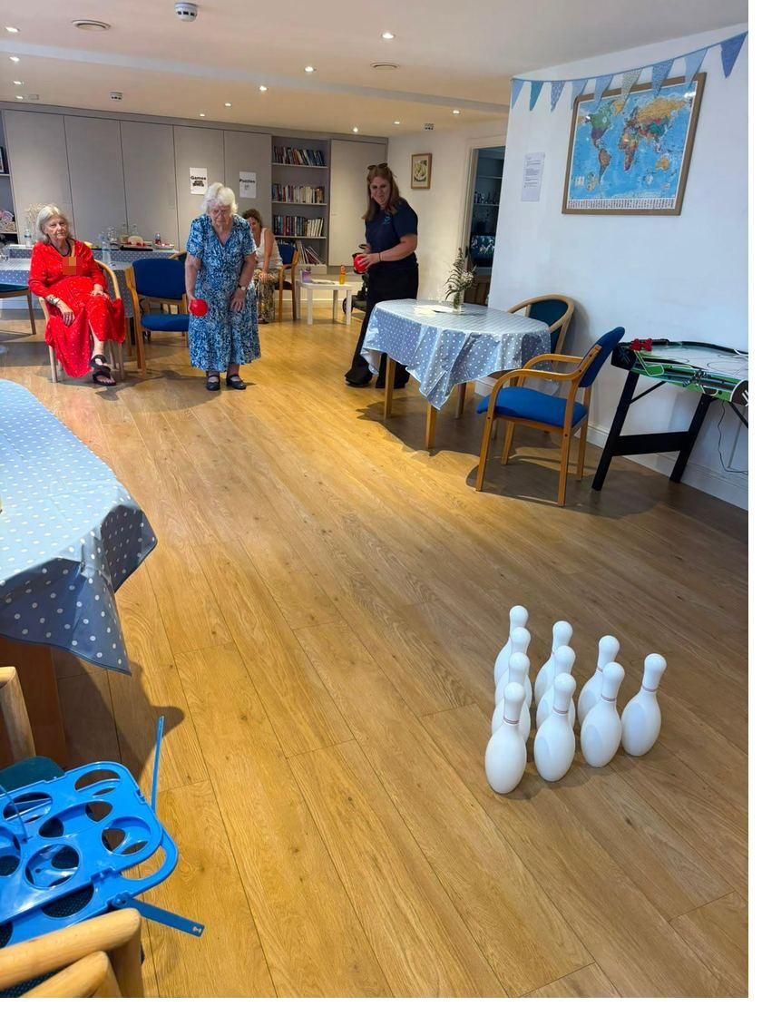 A lady bowling a ball at a set of skittles across the floor of the main room