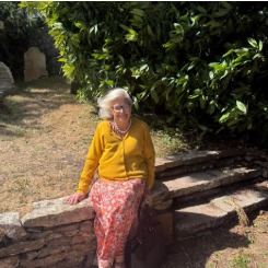 A lady in a yellow cardigan sitting on a sunlit churchyard wall